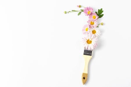 floral creative concept. paintbrush and pink paint. fresh flowers, buds and chrysanthemum leaves on white background. top view, copy space.の写真素材