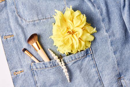 makeup brushes, pearl hair clips, yellow flower on blue denim background. creative concept, top viewの写真素材