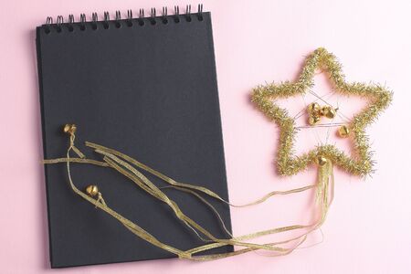 Layout for holiday to-do list. black notebook and star of tinsel on pink background. top view, copi...