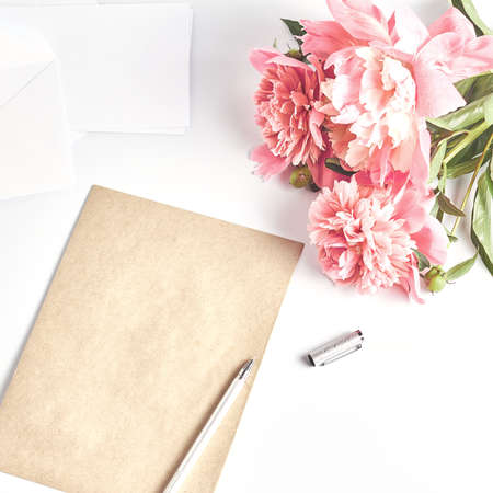 beautiful pink peony flower on a white desktop. envelopes and craft paper, a gray coffee mug. women...