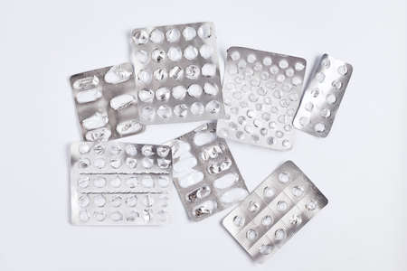 empty blister packs of pills with one partially full pack on white background. flat lay simple...