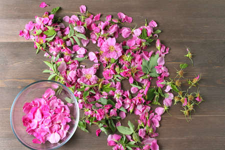 rose petals in a glass bowl on the background of lying pink flowers for drying on wood table.の写真素材