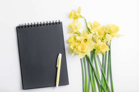 minimalistic workspace. white work desk with notepad black paper, pen and bouquet flower. top view, flat lay.の写真素材