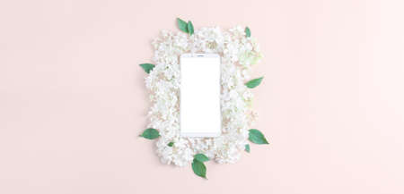 a beautiful composition of white hydrangea flowers on a beige background. smartphone with a blank screen. minimal layout, flat lay, long banner.の写真素材