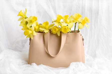 modern spring still life. bouquet of yellow daffodils in a beige womens bag on a white background. close-up.の写真素材