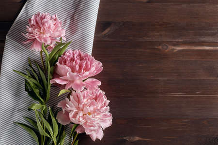 delicate pink peony flowers bouquet on a kitchen towel on a dark wooden background. simple flat composition with place for text. top view, copy space.の写真素材