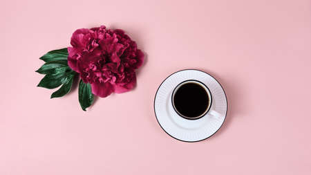 simple minimalistic composition with peony flower and coffee mug on pink background. workplace top view, panoramic banner with copy space.の写真素材