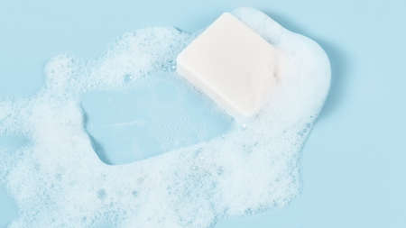 hand made soap in lush white foam on a light blue background. cosmetic background panoramic banner.の写真素材
