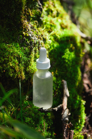 A clear dropper bottle is placed on vibrant green moss nestled within a serene forest, surrounded by nature's tranquility.の写真素材
