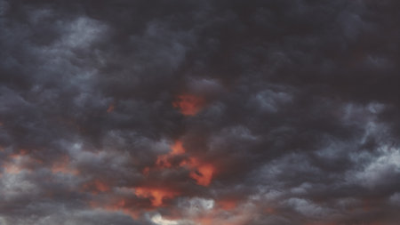Dark clouds mingle with hints of crimson and orange as twilight approaches, creating a dramatic...