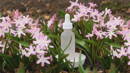 A dropper bottle stands upright in a lush garden filled with vibrant pink flowers, showing natures beauty.の写真素材