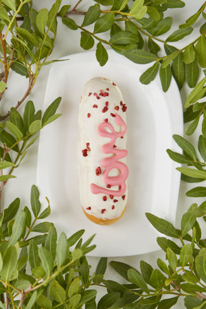A tasty donut features white frosting with pink love lettering, elegantly placed on a plate bordered...