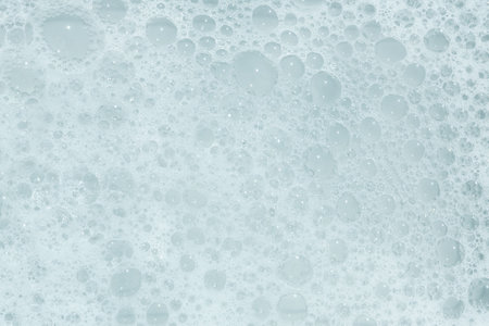 A close-up view captures the intricate details of bubbles forming in a foamy liquid. The soft, white...