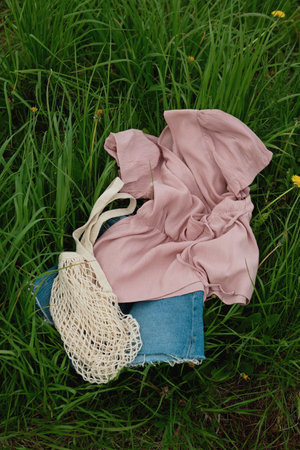 Perfect for a summer fashion mockup. Pink blouse, blue denim shorts and mesh bag lie on the green...