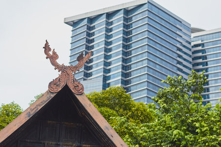 Intricate woodwork peaks from an open-roof structure while a contemporary building rises in the background amid lush greenery.の写真素材