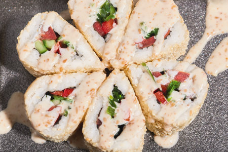 Six sushi rolls are neatly arranged in a circular pattern, featuring bright fillings of red and green vegetables, topped with a creamy sauce.の写真素材