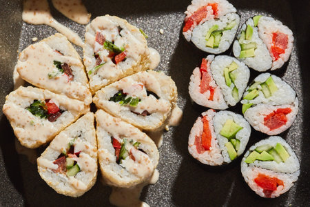 A variety of sushi rolls, including ones filled with fresh vegetables and seafood, are presented on a black plate, highlighting their vibrant colors and textures.の写真素材