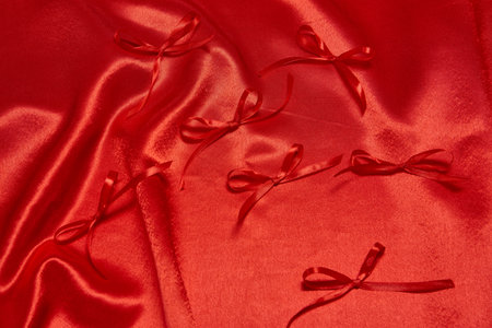 Soft red satin drapes elegantly, featuring delicate red bows arranged artfully, perfect for decorations or craft projects.の写真素材