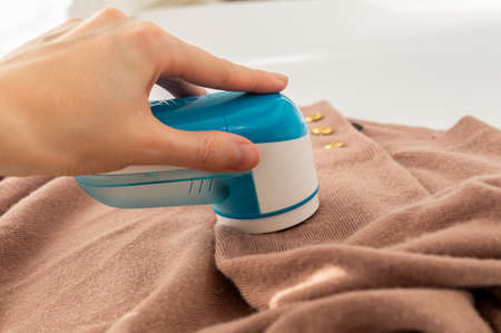 A young woman using a portable razor, trimmer, device to remove pellets, lint, fluff. Clothing care. Slow fashion. Longer use of clothingの写真素材