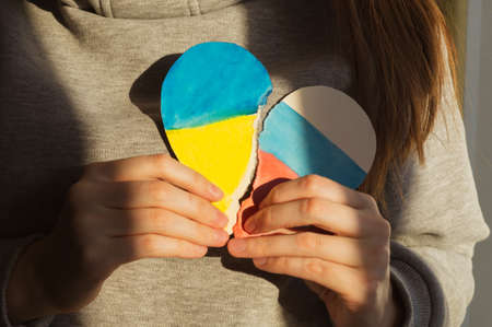Unrecognizable young caucasian woman holding a paper heart with the flag of Ukraine and Russia in her hands, military conflict february 2022の写真素材