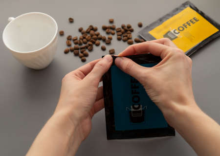 A young woman preparing a modern filter coffee in a drip bag at home. Step 1: Open the package.の写真素材