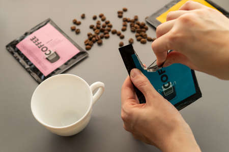 A young woman preparing a modern filter coffee in a drip bag at home. Step 1: Open the package.の写真素材