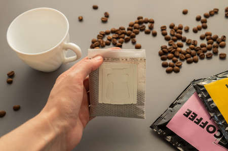 Young woman preparing a modern filter coffee in a drip bag at home. Step 2: Open drip bagの写真素材
