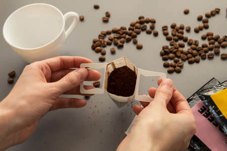 Young woman preparing a modern filter coffee in a drip bag at home. Step 2: Open drip bagの写真素材