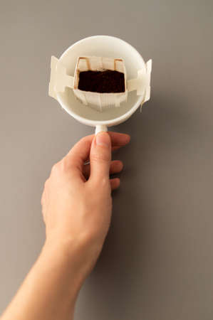 Cropped image of a young woman holding in her hand a white cup for making natural filter coffee in a drip bagの写真素材