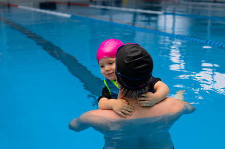 Father helping his little daughter overcome fear of swimming. Young father teaching his fearful daughter how to swim in swimming pool.の写真素材