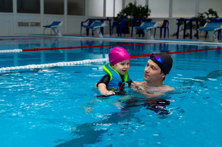 Happy father enjoying teaching his little daughter how to swim in swimming pool. Concept of health and a happy family.の写真素材