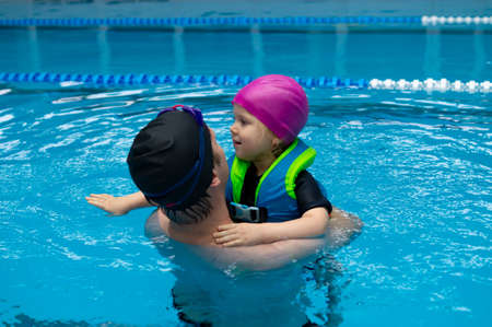 Father helping his little daughter overcome fear of swimming. Young father teaching his fearful daughter how to swim in swimming pool.の写真素材