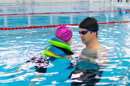 Happy father enjoying teaching his little daughter how to swim in swimming pool. Concept of health and happy family.の写真素材