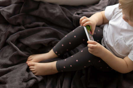 Top view of a little girl sitting on the window in a gray blanket and watching cartoons on her mobile phone.の写真素材