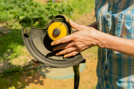 Unrecognizable senior woman cleaning a lawn mower from grass after work