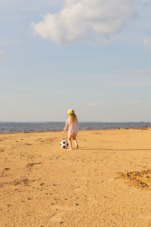 Little charming girl running barefoot on the sandy shore, playing a ball on the beach in active games and football. Trend for local tourism and regional travel.の写真素材