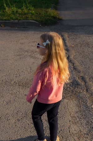 A cute little girl in sunglasses with long blonde hair walking in an autumn park.の写真素材