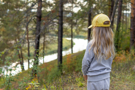 Portrait of an adorable little girl in a yellow cap and with long natural hair on a walk by the river in the autumn forest.の写真素材