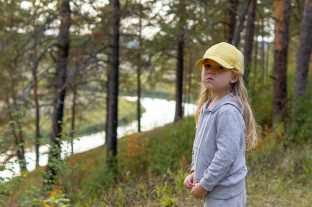 Portrait of a little cute serious girl is walking in a beautiful forest in the autumn near the river.の写真素材