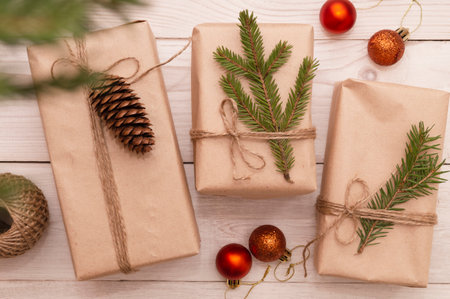 Creative DIY hobby. Making a modern handmade Christmas gift on a white wooden background. Boxes of brown craft paper, jute twine, linen rope, fir branches, Christmas balls, present decorations. Top view, DIY conceptの写真素材