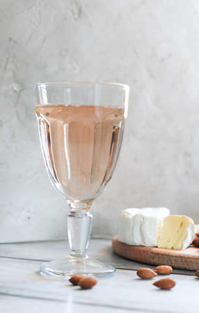 Glass of rose wine with brie cheese and almonds on the light concrete background. Vertical...