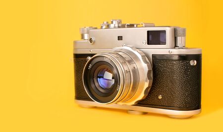 Retro, vintage film photo camera isolated on yellow colourful trendy modern fashion background. Camera lens with reflections. Film camera. Creative, minimalismの写真素材