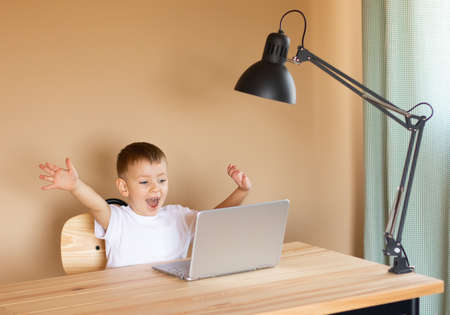 The child sits at the computer, rejoices and laughs.の写真素材