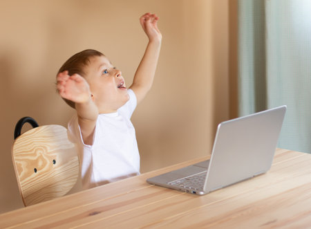 The child sits at the computer, rejoices and laughs.の写真素材