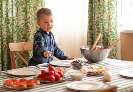 Little blond boy at a feast, choosing food. A festively laid table, Christmas, New Year, Birthday Eveの写真素材