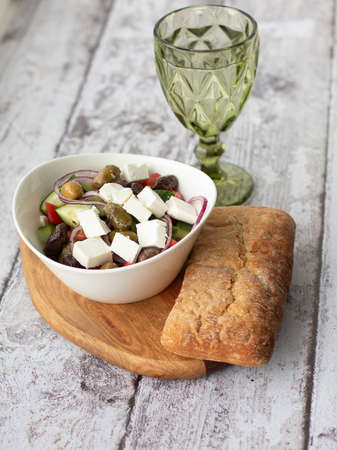Mediterranean cuisine concept. Greek salad in white bowl and glass of water on the wooden background.の写真素材
