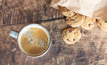 Chocolate chip cookies and cup of coffee in craft bag on wooden background