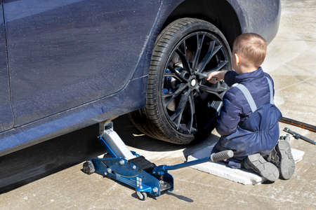 A little boy fixes a car, changes a wheel, helps his dad.の写真素材