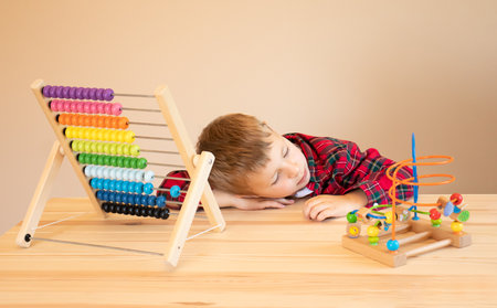 Little tired boy sits at the table and plays with wooden educational toys, put his head on the table and fell asleep.の写真素材