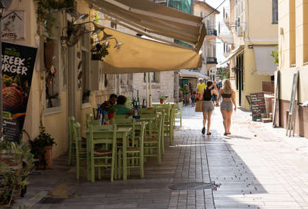 07.16.2021, Nafplio, Greece. Narrow streets of Nafplio town, tavern with green chairsのeditorial素材